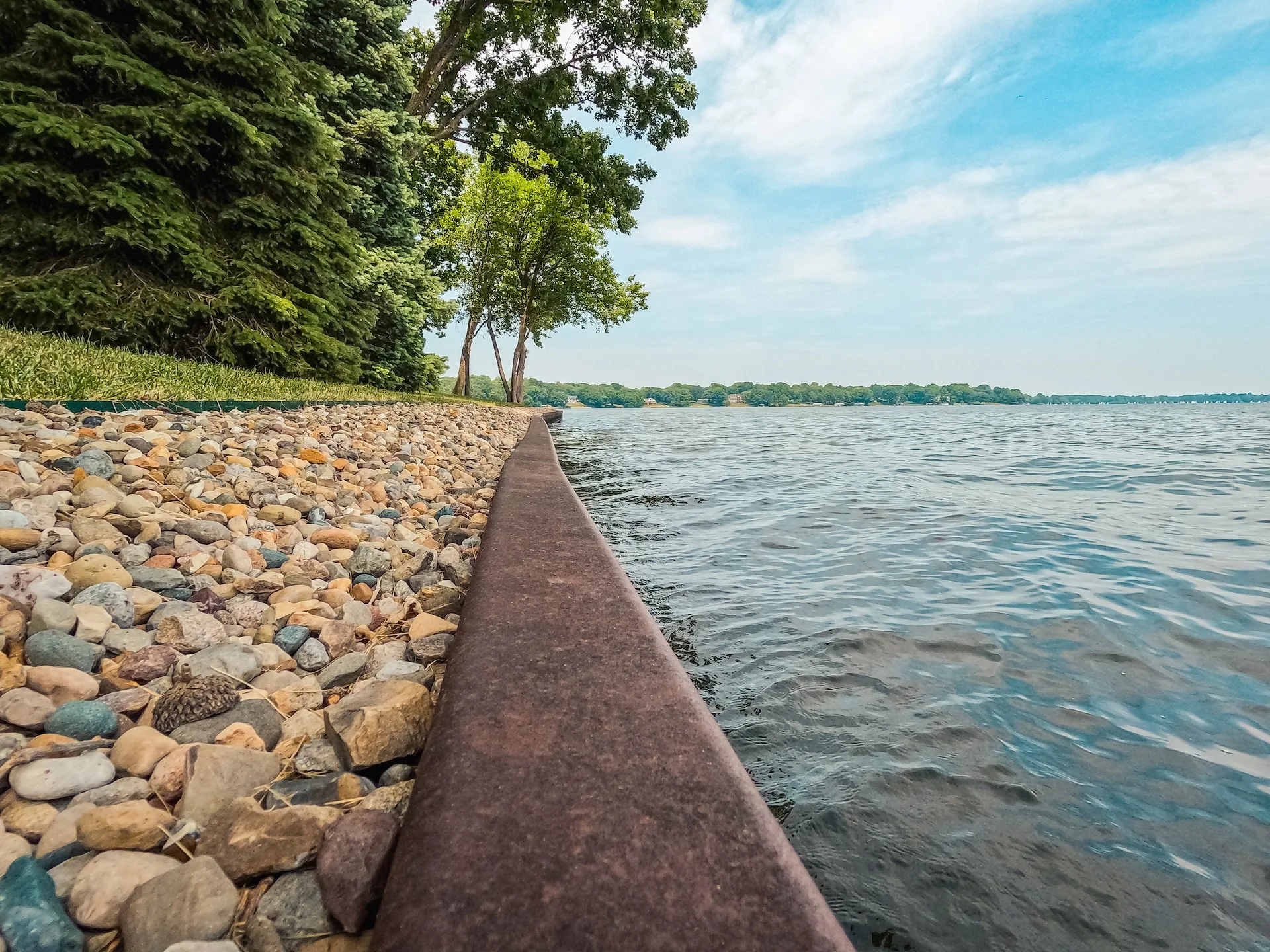 Surface Level View Of A Metal Retaining Wall Dividing The Lake From The Land. An Ornamental Stone Path Runs Along The Retaining Wall. A Retaining Wall Is Used To Protect Land From Soil Erosion.